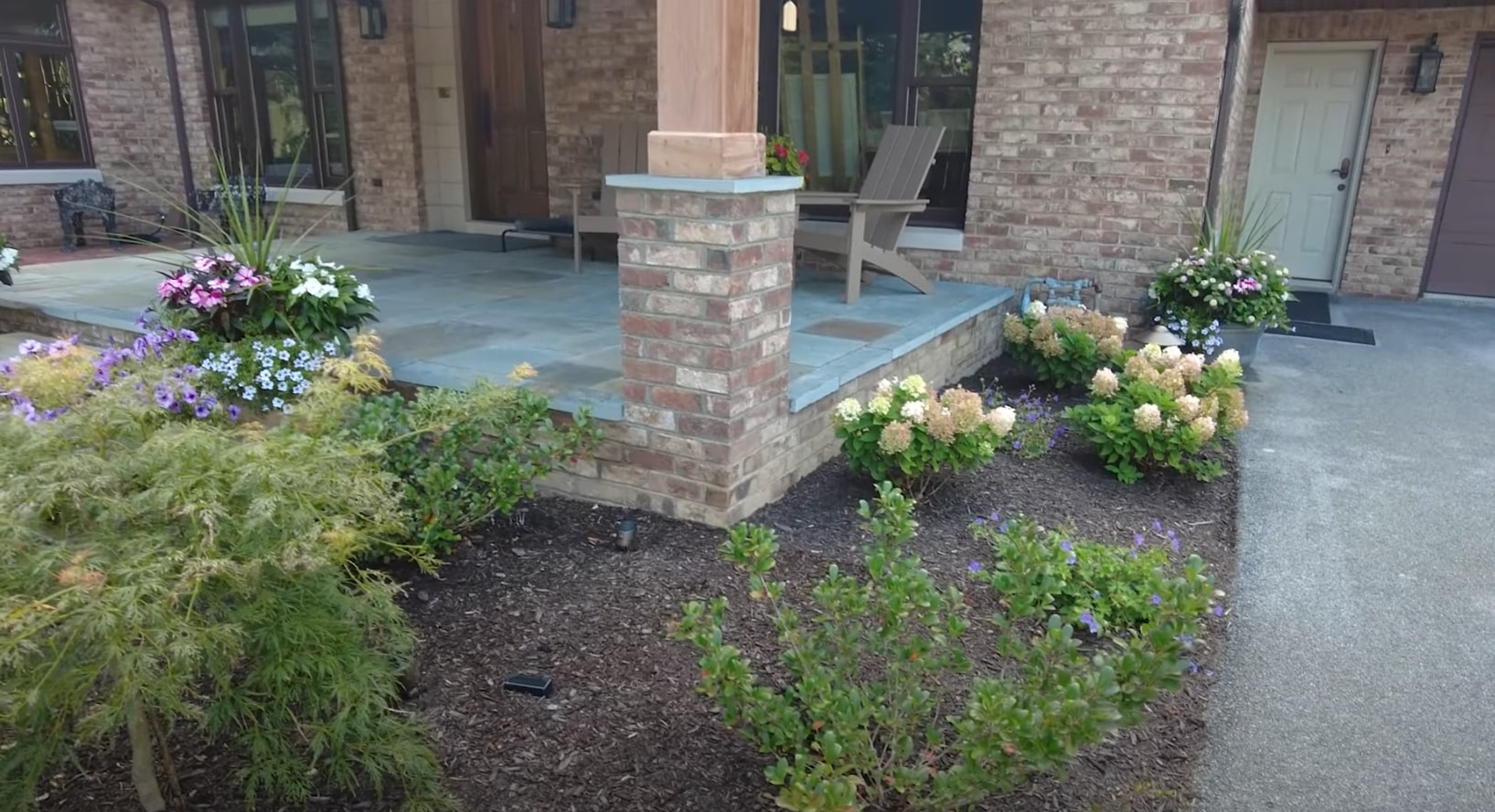 Front Patio Hardscaping Design Professional front patio hardscaping with brick columns, stone planters, and colorful flower beds